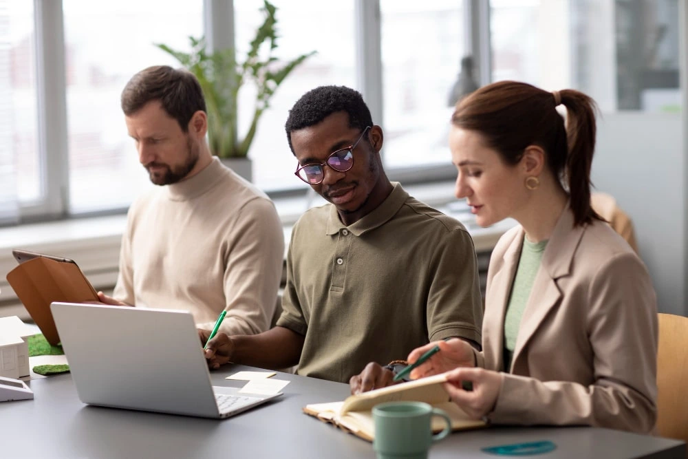 Two men and a woman working together while using digital devices in an office setting.