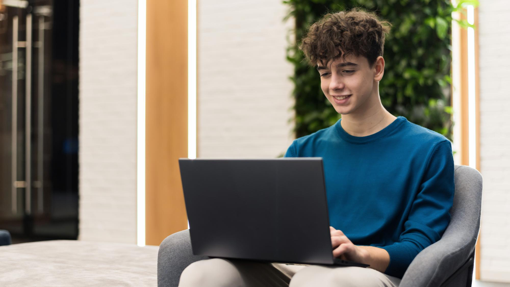 A young man working on a laptop in an outdoor seating setting.